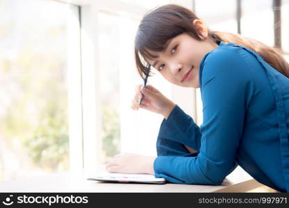 Beautiful portrait young asian woman writer smiling thinking idea and writing on notebook or diary with happy, lifestyle of asia girl is student, female planning working, education and business concept.