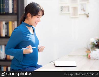 Beautiful portrait young asian woman writer writing on notebook or diary with happy and excited, lifestyle asia girl planning working and success, education and business concept.
