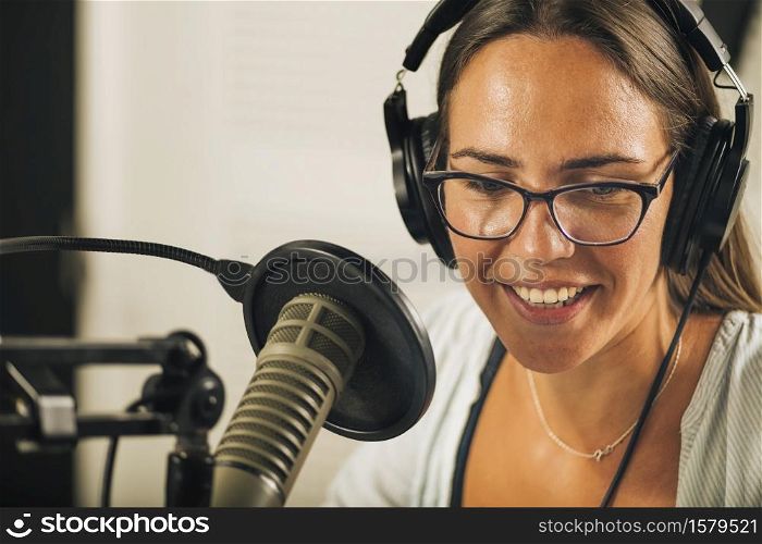 Beautiful positive young woman podcasting from her studio, wearing headphones, talking to the microphone. Podcasting