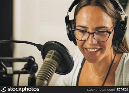 Beautiful positive young woman podcasting from her studio, wearing headphones, talking to the microphone. Podcasting