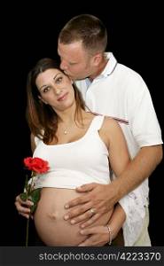 Beautiful pregnant couple. He&rsquo;s touching her belly and kissing her on the cheek. Black background.
