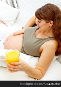 Beautiful pregnant female relaxing on sofa at home with glass of juice in hand&#xA;