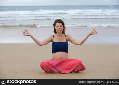 Beautiful pregnant girl practicing yoga on the beach