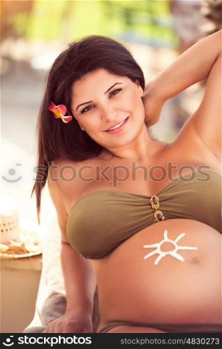Beautiful pregnant girl spending time on the tropical beach resort, enjoying sunny day, using sunscreen, happy healthy pregnancy