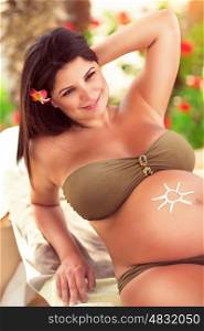Beautiful pregnant girl spending time on the tropical beach resort, enjoying sunny day, using sunscreen, happy healthy pregnancy