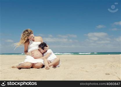 Beautiful pregnant woman and her little daughter kissing mom&rsquo;s belly