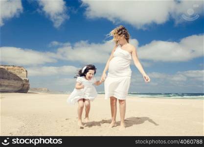Beautiful pregnant woman and her little daughter playing on the beach