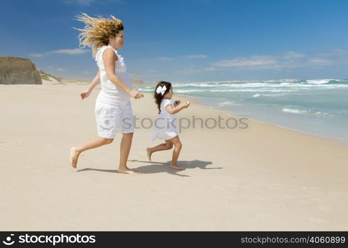 Beautiful pregnant woman and her little daughter running to the sea