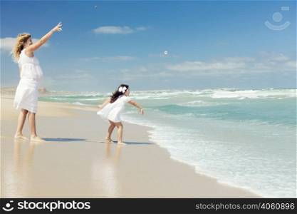 Beautiful pregnant woman and her little daughter throwing stones on the beach