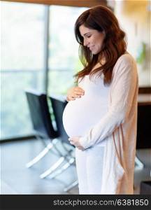 Beautiful pregnant woman at home, happy anticipation of baby, calm female touching her tummy and looking on it with love
