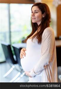 Beautiful pregnant woman at home, happy anticipation of baby, calm female touching tummy and dreamy looking away