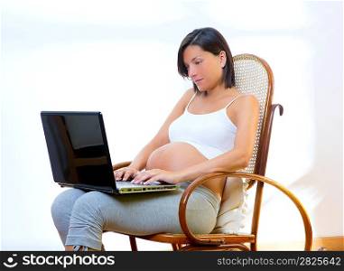 Beautiful pregnant woman at home with laptop computer on rocker chair