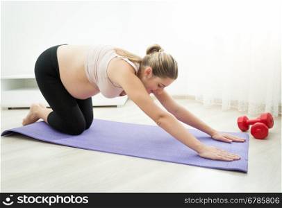 Beautiful pregnant woman doing yoga exercises on fitness mat at living room