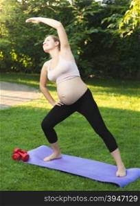 Beautiful pregnant woman exercising on green grass at park
