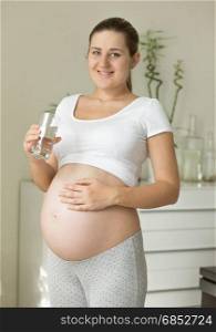 Beautiful pregnant woman holding glass of water and looking on belly