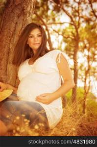Beautiful pregnant woman in spending time autumn forest, sitting down on dry yellow grass, happy pregnancy, loving family concept