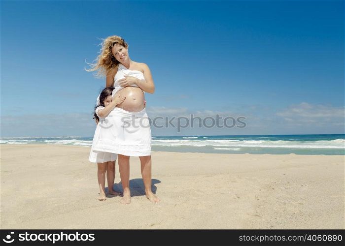 Beautiful pregnant woman in the beach with her little daughter applying sunscreen on mom&rsquo;s belly