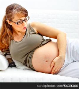 Beautiful pregnant woman lying on sofa at home and holding her belly.&#xA;