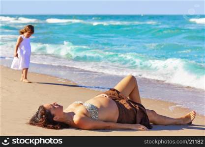 Beautiful pregnant woman on the beach lying with daughter