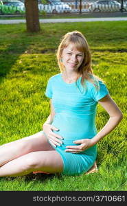 Beautiful pregnant woman relaxing in the park on a grass