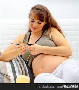 Beautiful pregnant woman sitting on sofa and knitting for her baby.&#xA;