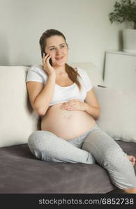 Beautiful pregnant woman sitting on sofa and talking by phone