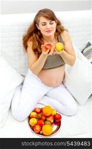 Beautiful pregnant woman sitting on sofa at home and enjoying fruits&#xA;