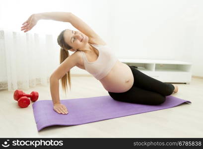 Beautiful pregnant woman stretching on fitness mat at home