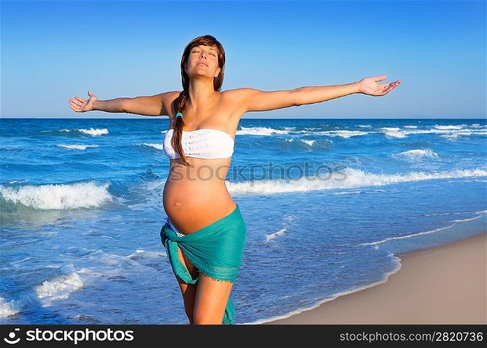 Beautiful pregnant woman walking on blue beach in summer vacation with open arms