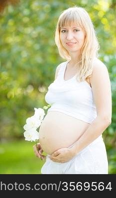 Beautiful pregnant woman with flower against green spring background