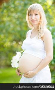 Beautiful pregnant woman with flower against green spring background