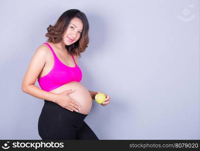 Beautiful pregnant woman with green apple on gray background