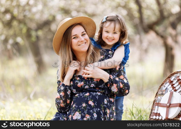 beautiful pregnant woman with little daughter playing on a picnic in a blooming spring garden.. beautiful pregnant woman with little daughter playing on a picnic in a blooming spring garden