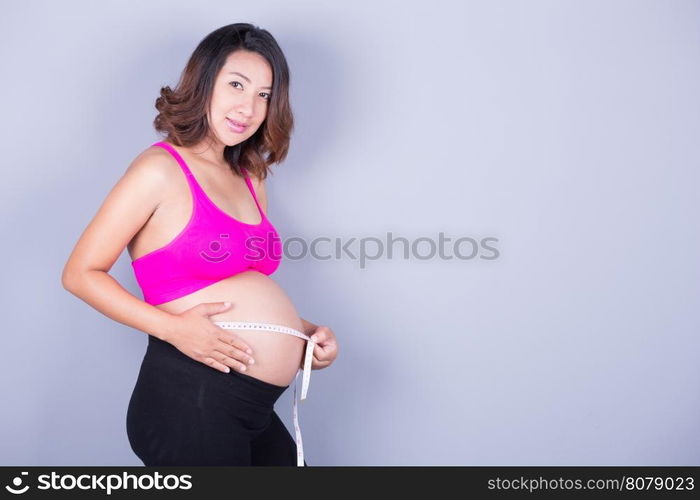 beautiful Pregnant woman with measuring tape on gray background