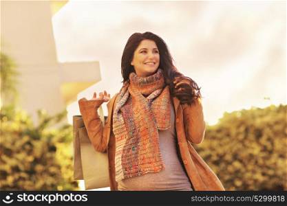 Beautiful pregnant woman with shopping bags outdoors, with pleasure expecting a baby and preparing, happy pregnancy time