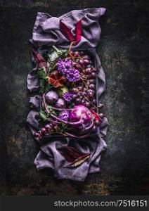 Beautiful purple fruit, vegetables and flowers composing on purple color tablecloth on dark background.Top view. Flat lay