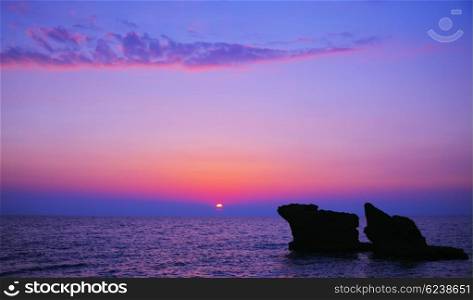 Beautiful purple sunset on the beach, seascape with calm ocean and rocks in the blue water