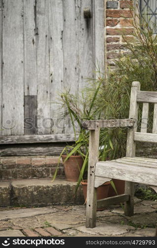 Beautiful quintessential old English country garden image of wooden chair next to vintage back door