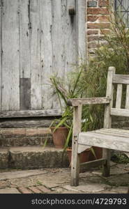 Beautiful quintessential old English country garden image of wooden chair next to vintage back door