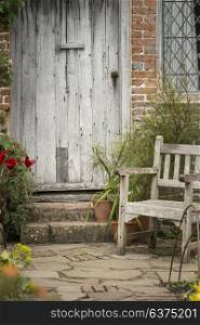 Beautiful quintessential old English country garden image of wooden chair next to vintage back door