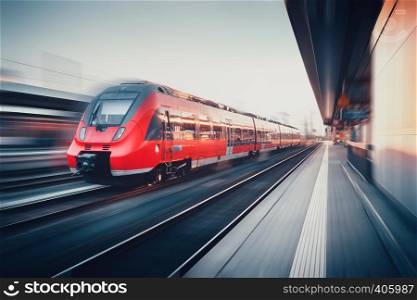 Beautiful railway station with modern high speed red commuter train with motion blur effect at sunset in Nuremberg, Germany. Railroad. Vintage toning. Railroad travel background, tourism. Industrial