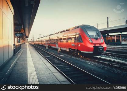 Beautiful railway station with modern red commuter train at colorful sunset in Nuremberg, Germany. Railroad with vintage toning