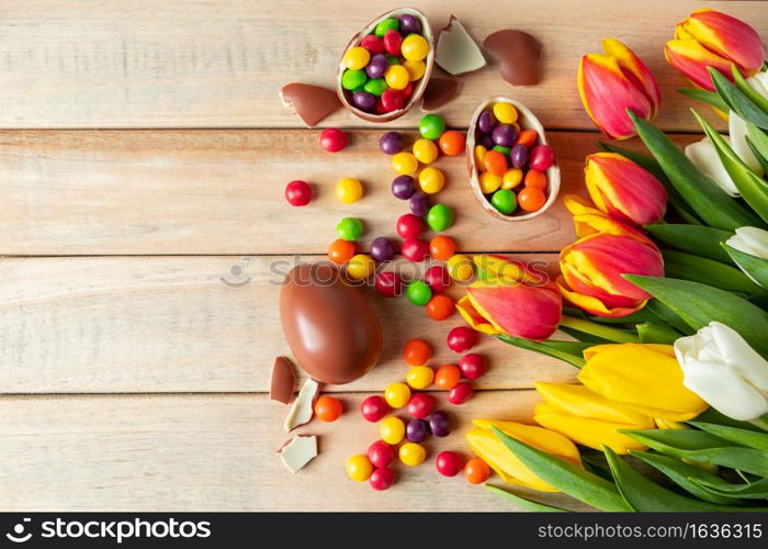 Beautiful red and yellow tulips for easter holiday. Chocolate eggs and candies on a wooden background. Festive design for postcards, copy space. Beautiful red and yellow tulips for easter holiday. Chocolate eggs and candies on a wooden background.