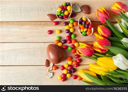Beautiful red and yellow tulips for easter holiday. Chocolate eggs and candies on a wooden background. Festive design for postcards, copy space. Beautiful red and yellow tulips for easter holiday. Chocolate eggs and candies on a wooden background.