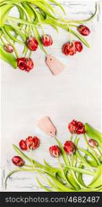 Beautiful red curved tulips with tags on white wooden background, top view, vertical floral border. Spring flowers concept