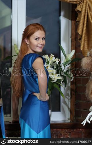 beautiful red-haired woman in a dress standing at the window