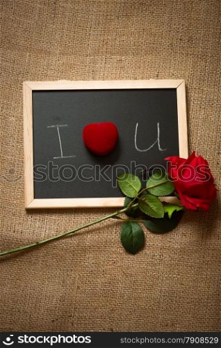 Beautiful red rose and ring in box lying on chalkboard