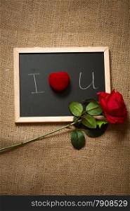 Beautiful red rose and ring in box lying on chalkboard