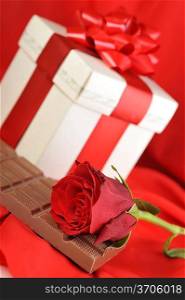 beautiful red rose, gift and chocolate on red close up