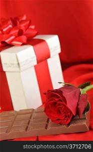 beautiful red rose, gift and chocolate on red close up